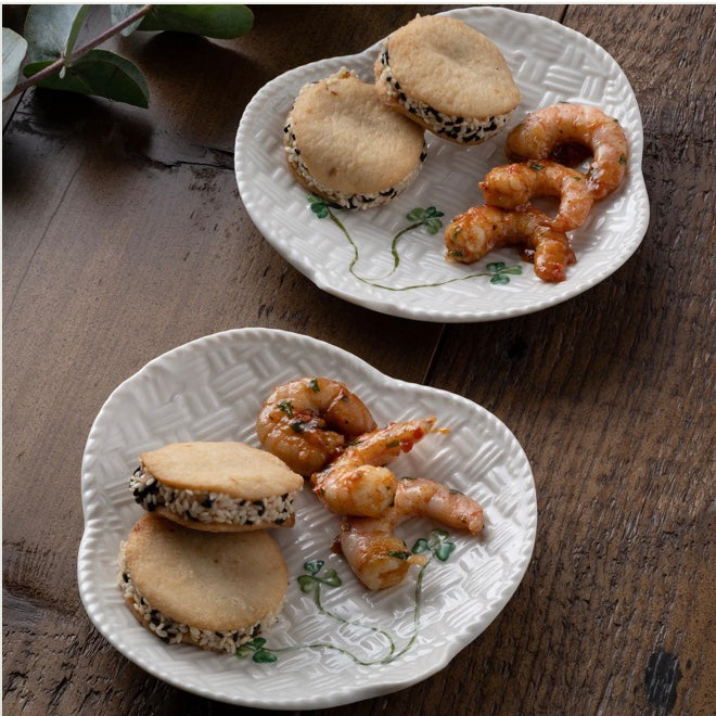 Two white decorative plates with shrimp and sandwich-like items on a wooden surface.
