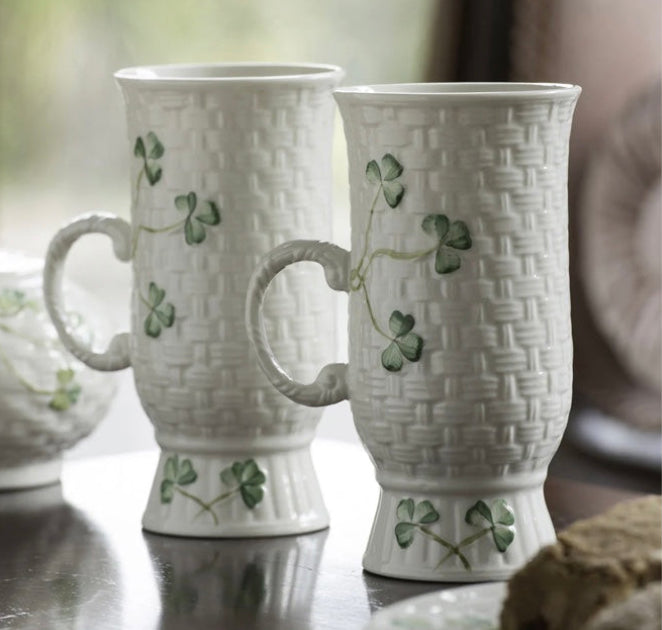 Two white ceramic mugs with woven pattern and clover design on a reflective surface.