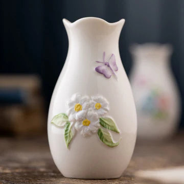 White ceramic vase with floral and butterfly design on a wooden surface
