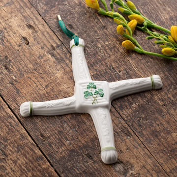 Decorative cross with a shamrock on a wooden surface with yellow flowers.