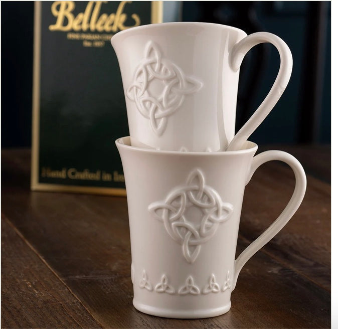 Two white ceramic mugs with Celtic knot design on a wooden surface, with a Belleek box in the background.
