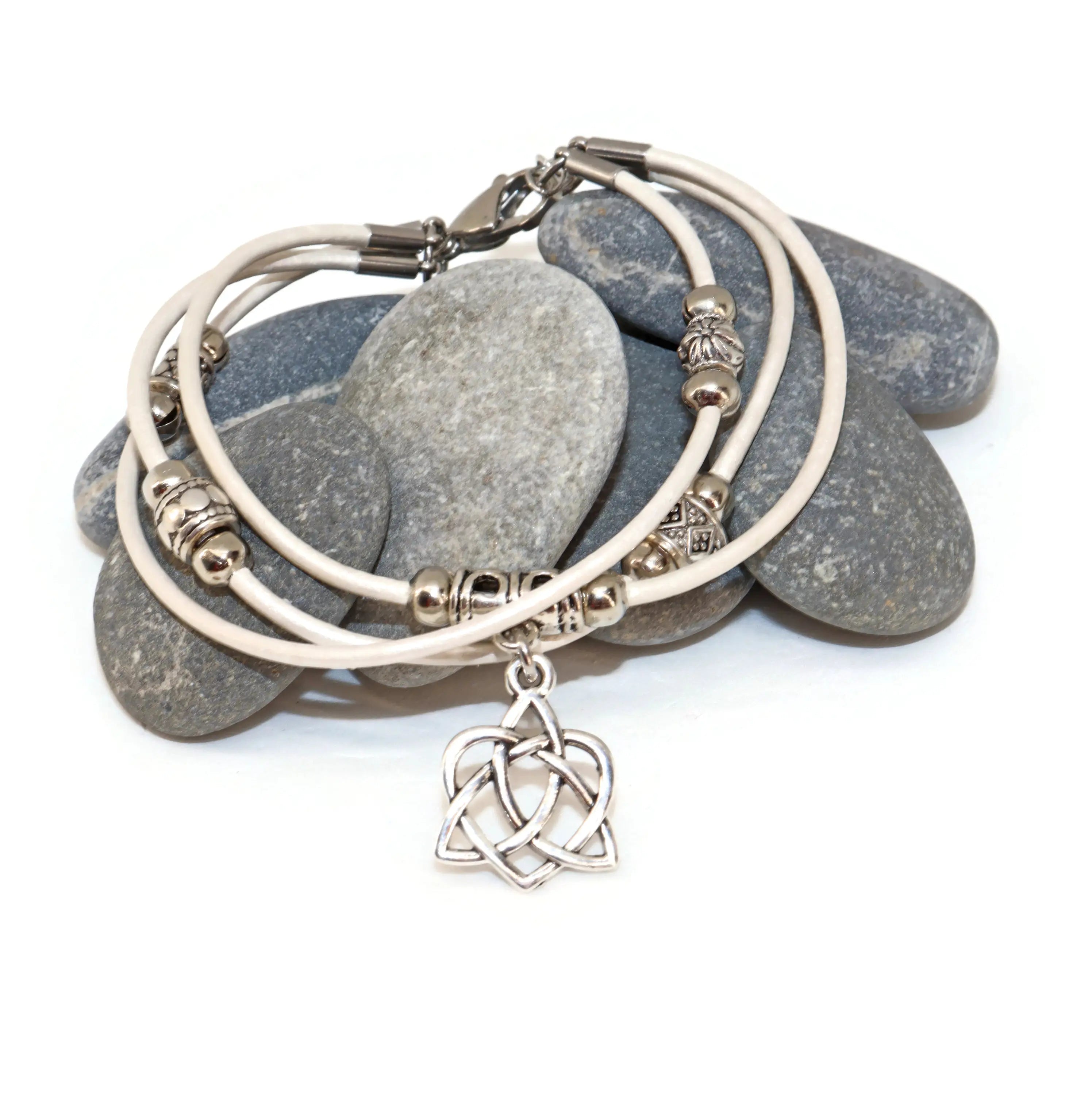 Stack of silver bracelets with a Celtic knot charm on a white background