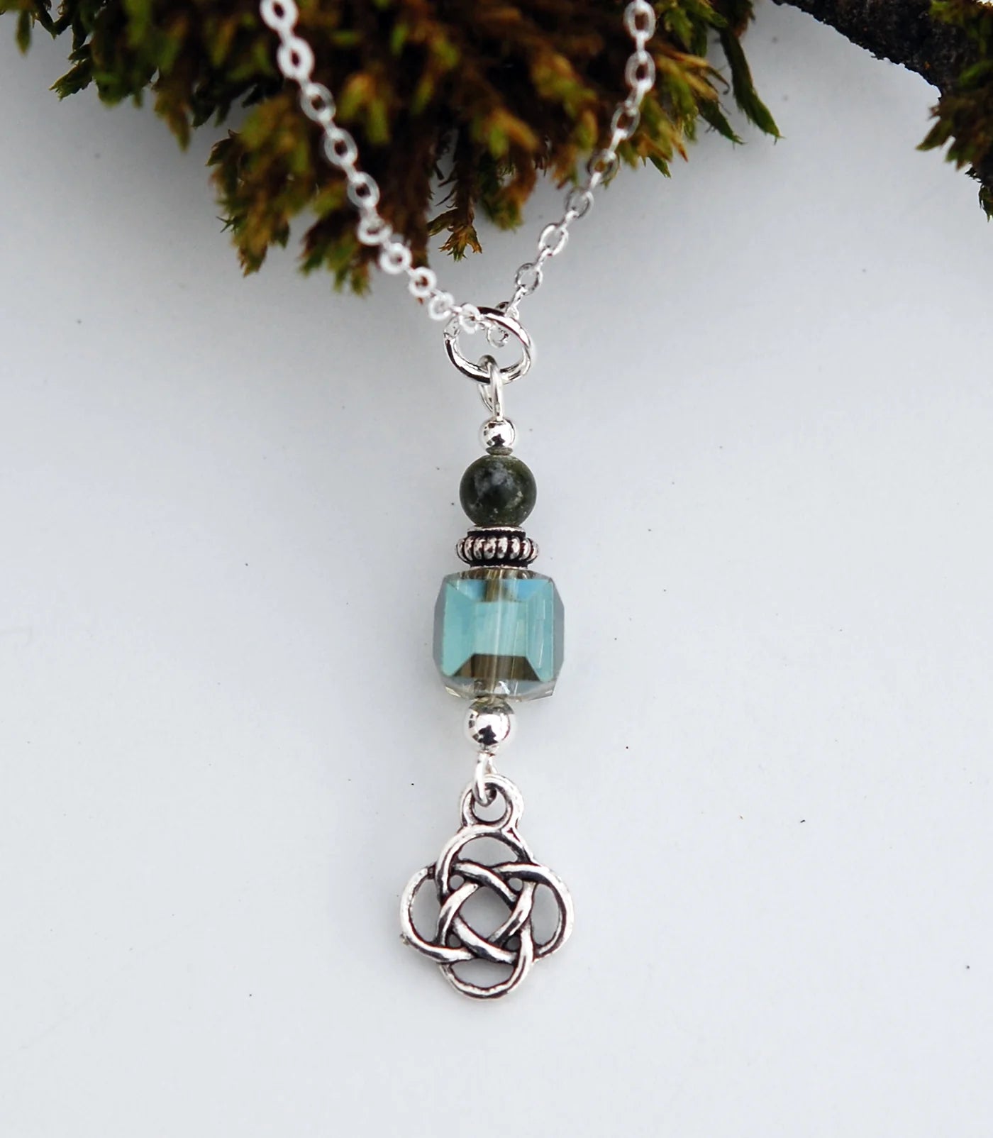 Necklace with a turquoise bead and silver Celtic knot pendant against a white background