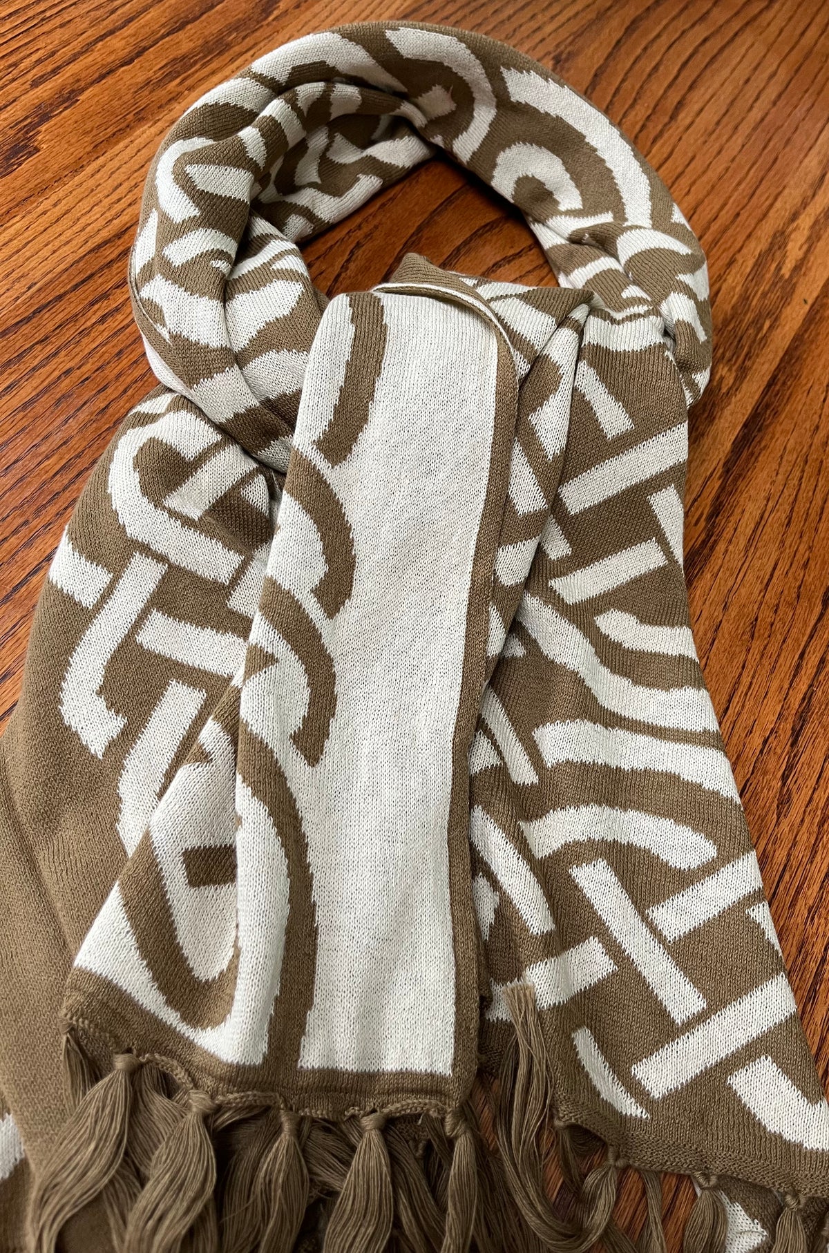 A knit scarf with a brown and off-white geometric pattern, laid flat on a wooden surface.
