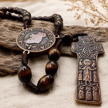 A dark brown wooden bead rosary with a round medallion and a detailed cross pendant, displayed on a piece of weathered wood over a beige fabric background.