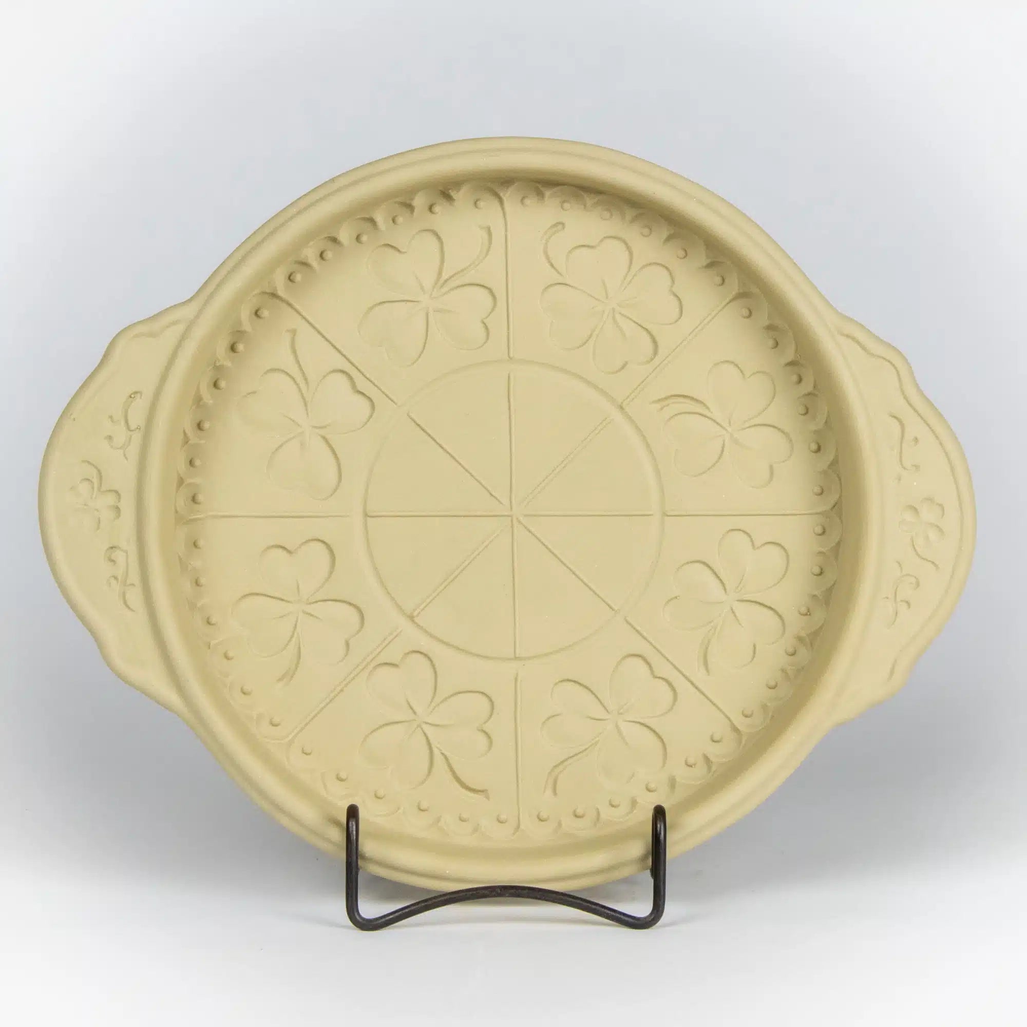 Decorative beige plate with embossed shamrock patterns on a stand against a white background