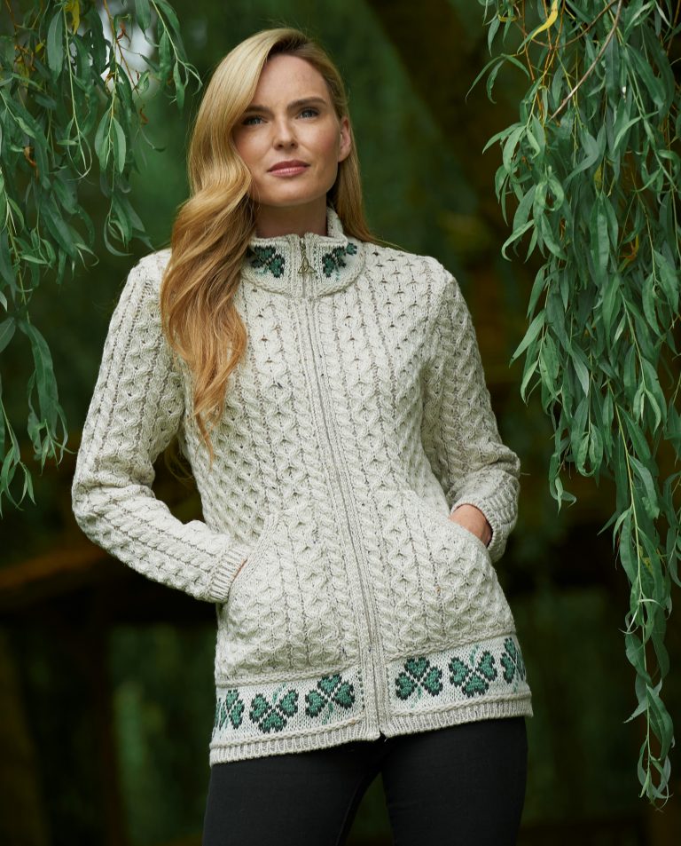 Woman wearing a cream-colored knit cardigan with green shamrock patterns against a natural background.