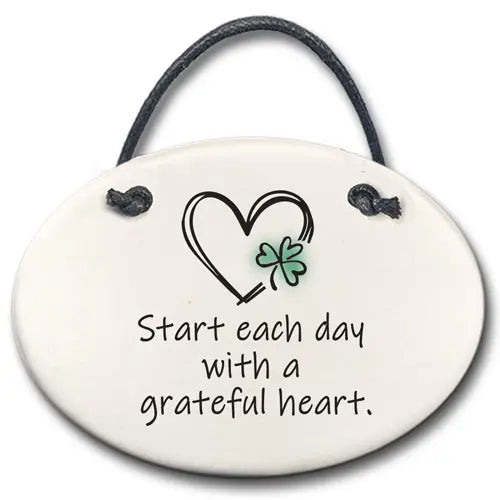 Decorative hanging plate with a heart and clover design and text 'Start each day with a grateful heart.'
