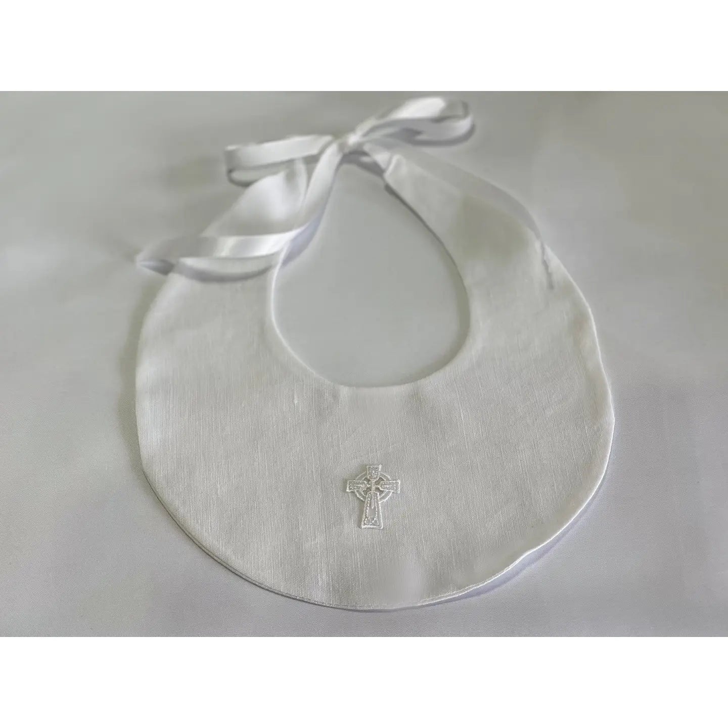 White bib with a cross design and satin ribbon on a light gray background