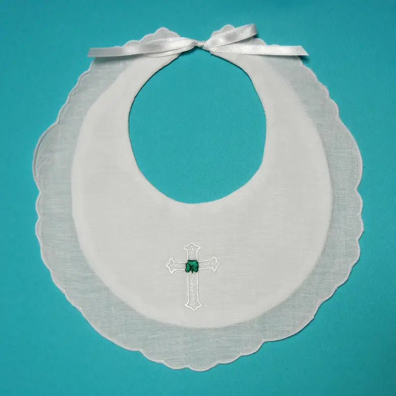White bib with scalloped edge and embroidered cross & shamrock on a teal background