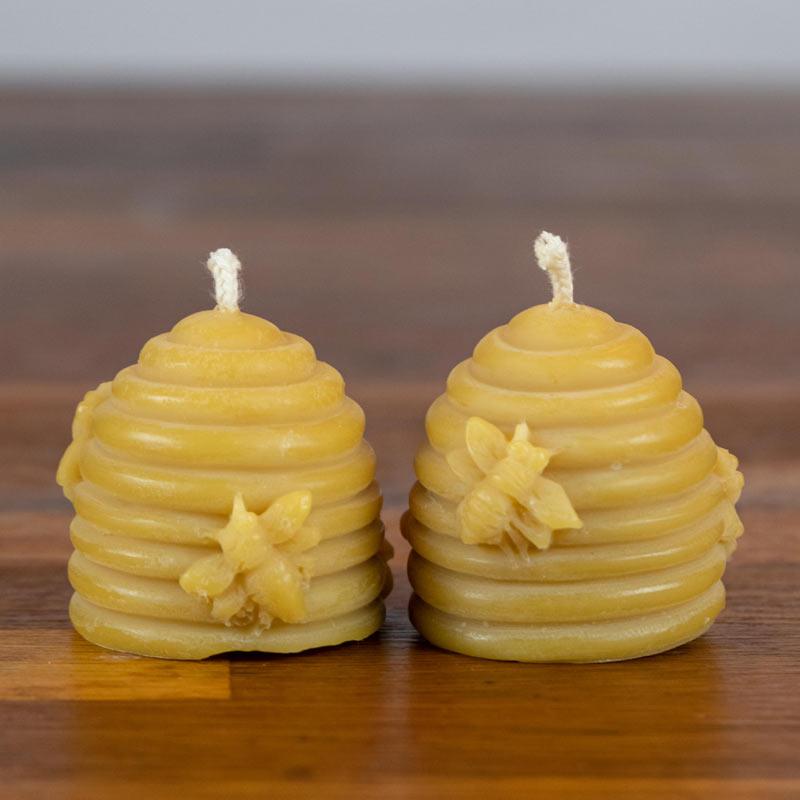 Two beehive-shaped candles with bee designs on a wooden surface