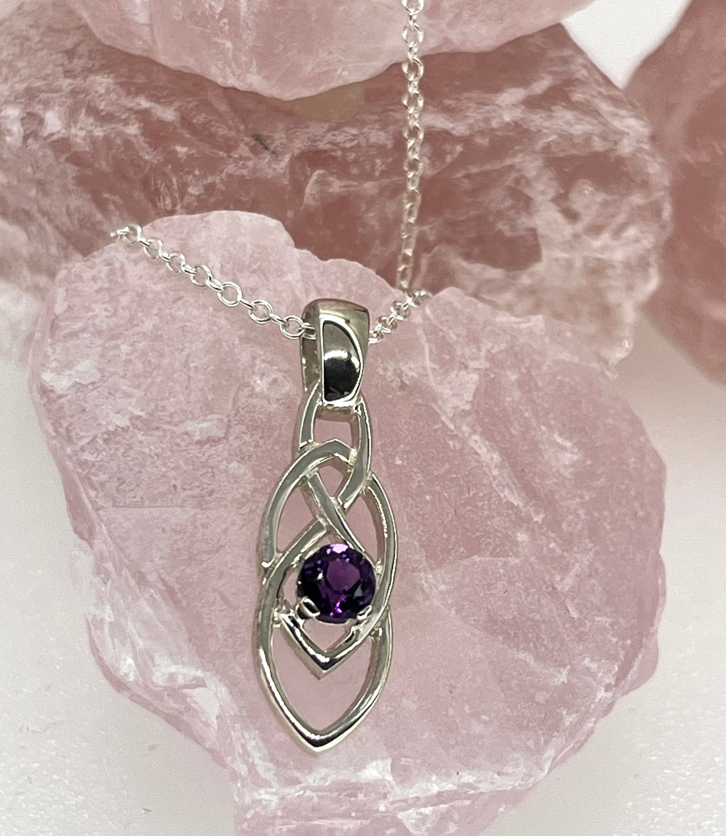 Silver pendant with a purple gemstone on a chain, set against a stone background