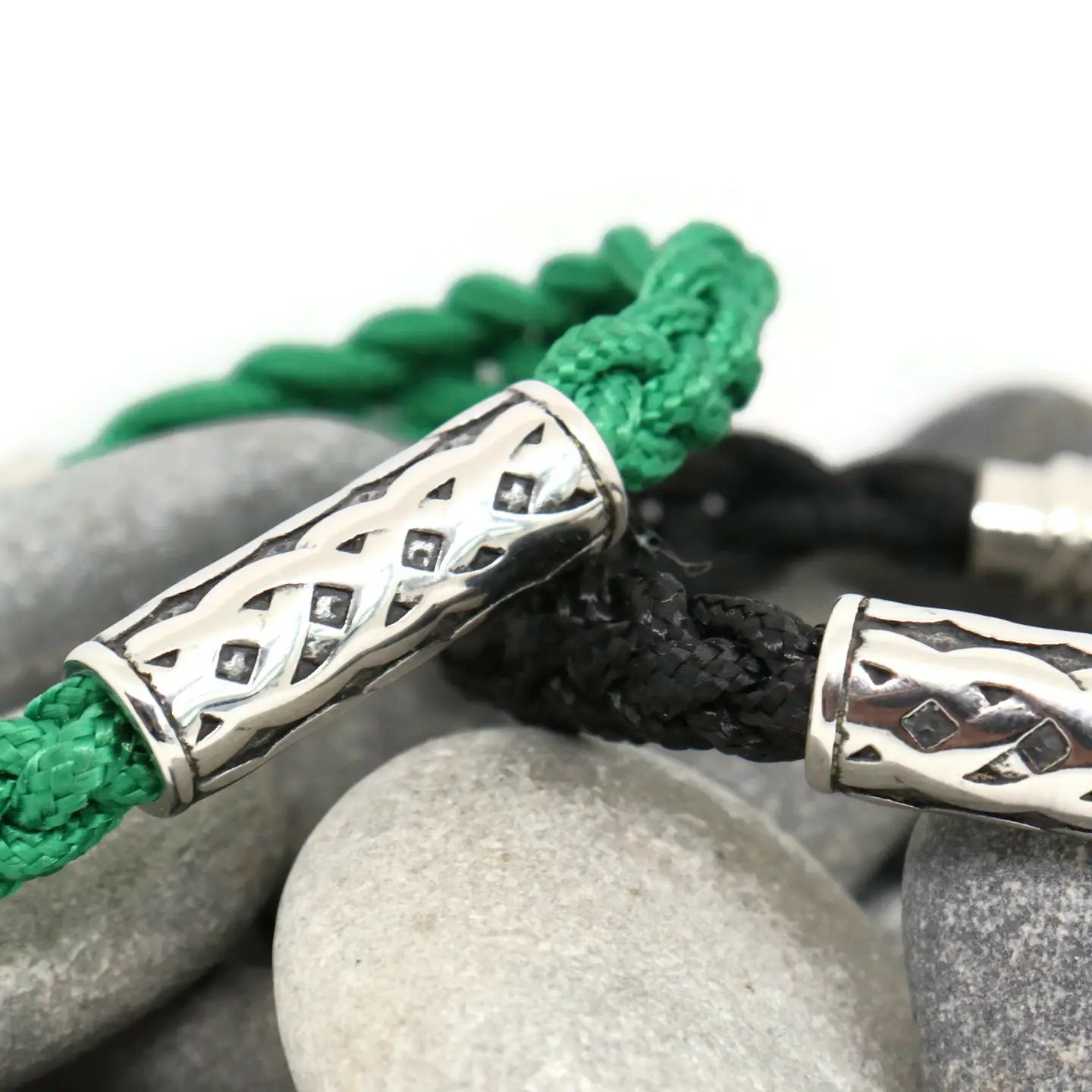 Bracelet with green and black braided cord and silver Celtic knot design on stones.