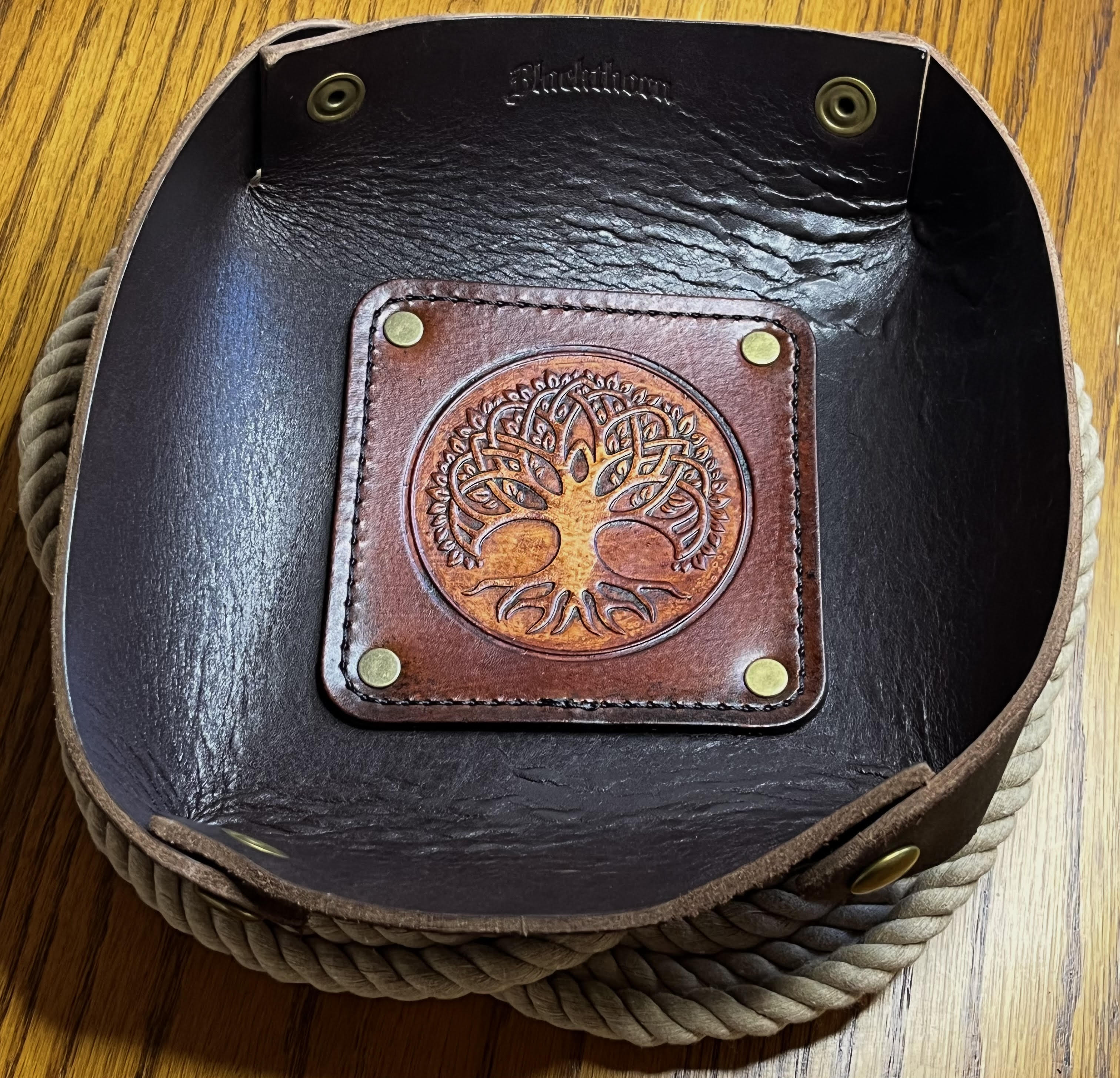 Brown leather tray with tree of life design on a wooden surface
