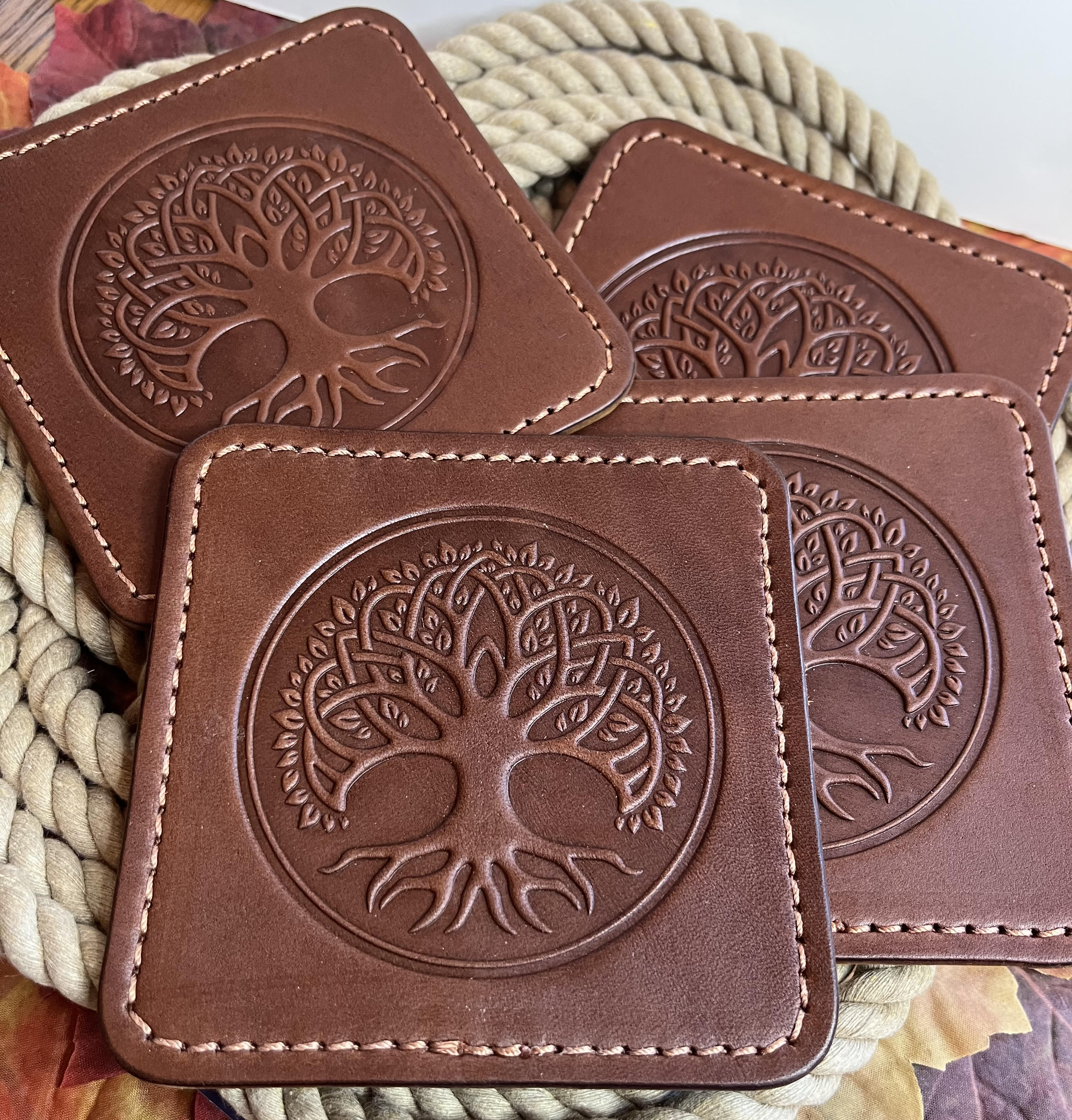 Brown leather coasters with tree of life design on a woven surface