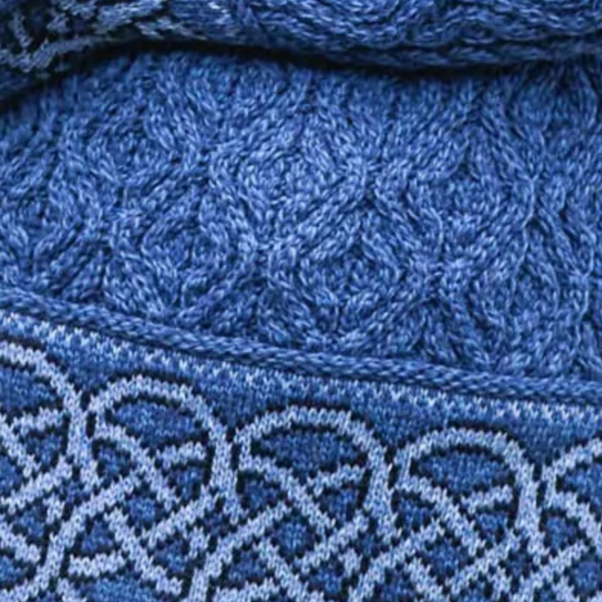 Close-up of a blue knitted textile with a textured cable-knit pattern and a contrasting light blue and navy woven border.