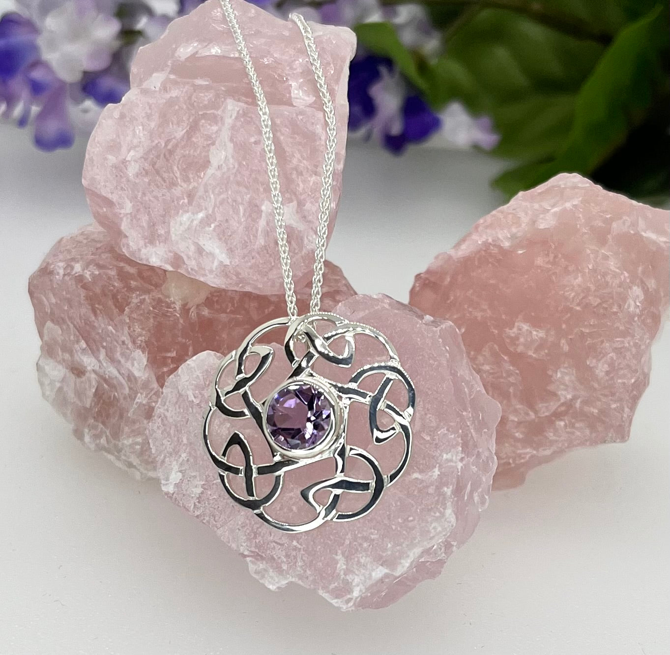 Silver necklace with a purple gemstone pendant on pink crystal stones.