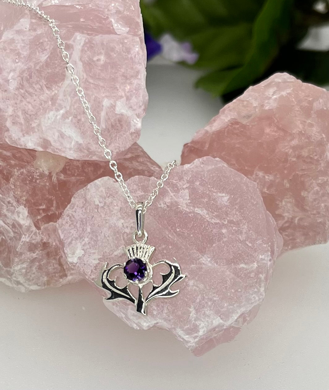 Silver necklace with a pendant featuring a purple gemstone, displayed on pink rose quartz crystals.