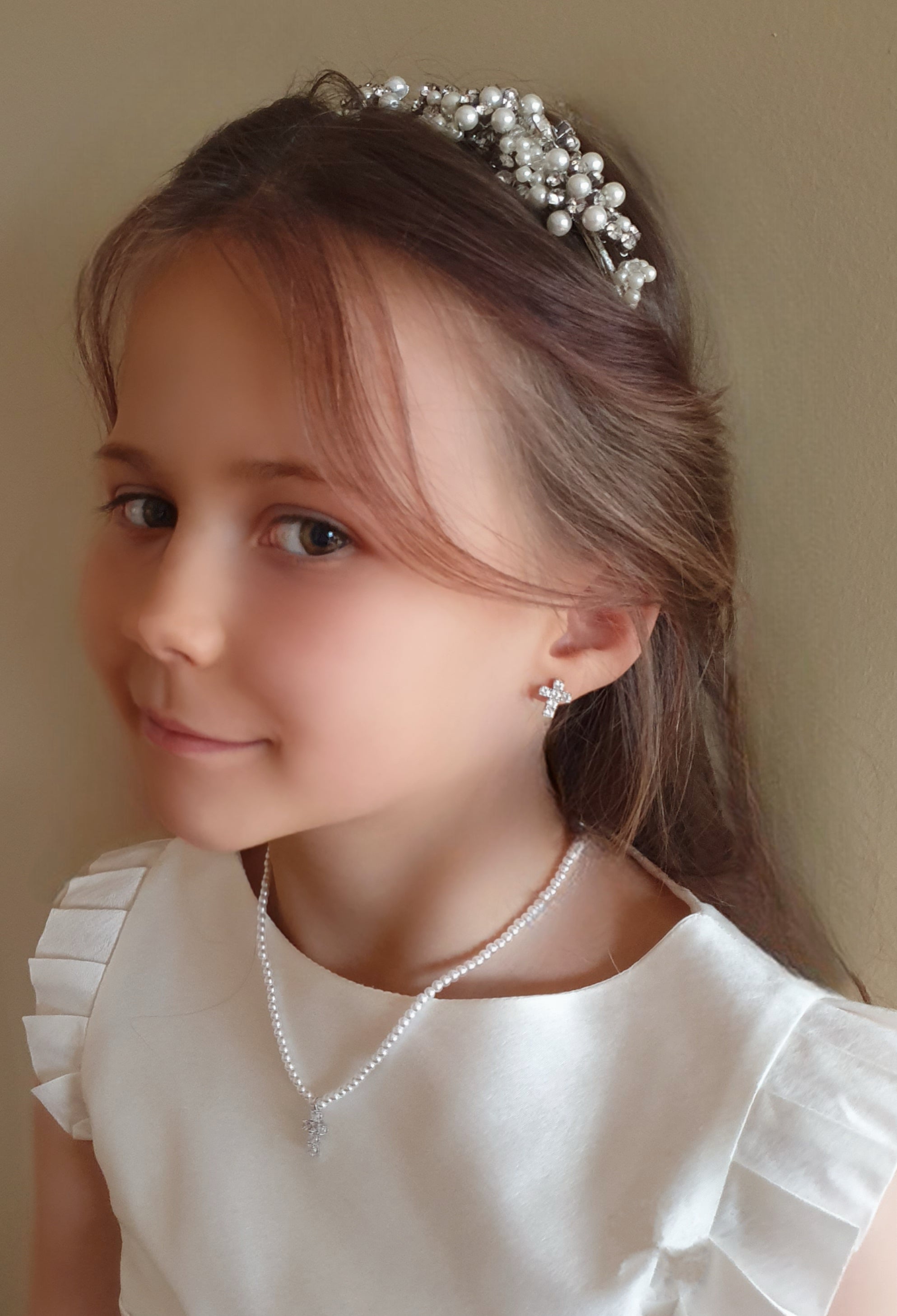 Young girl wearing a pearl tiara and necklace against a plain background
