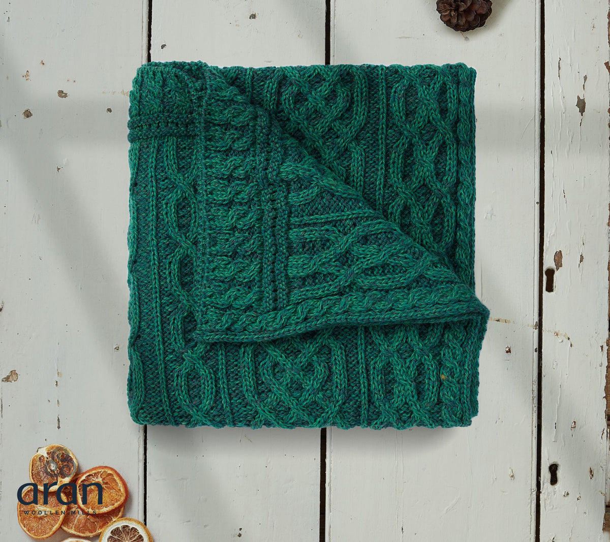 Folded green knitted blanket on a wooden surface with dried oranges and pine cones. Irish Aran Knit.