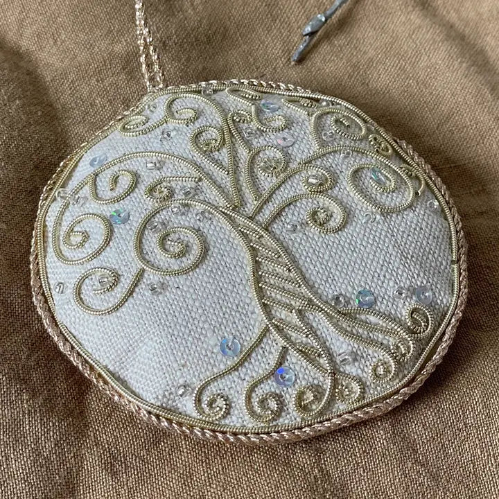 Embroidered tree of life design on a circular fabric piece with beads.