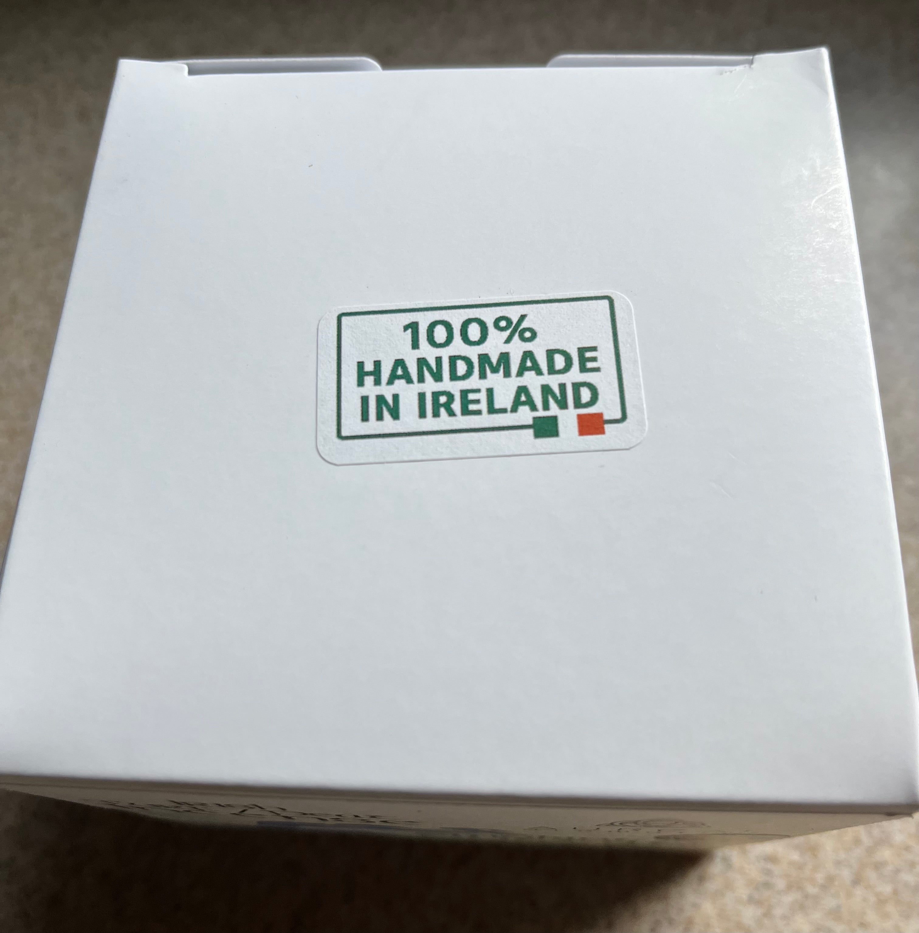 A white cardboard box with a sticker that reads '100% HANDMADE IN IRELAND' on a beige carpeted floor.
