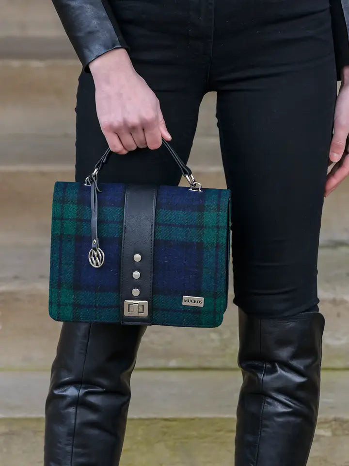 Person holding a blue and green plaid handbag with leather accents.
