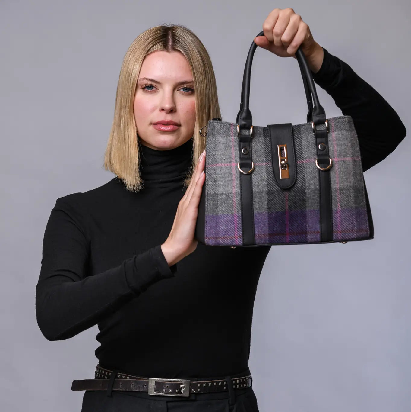Woman holding a plaid handbag against a gray background