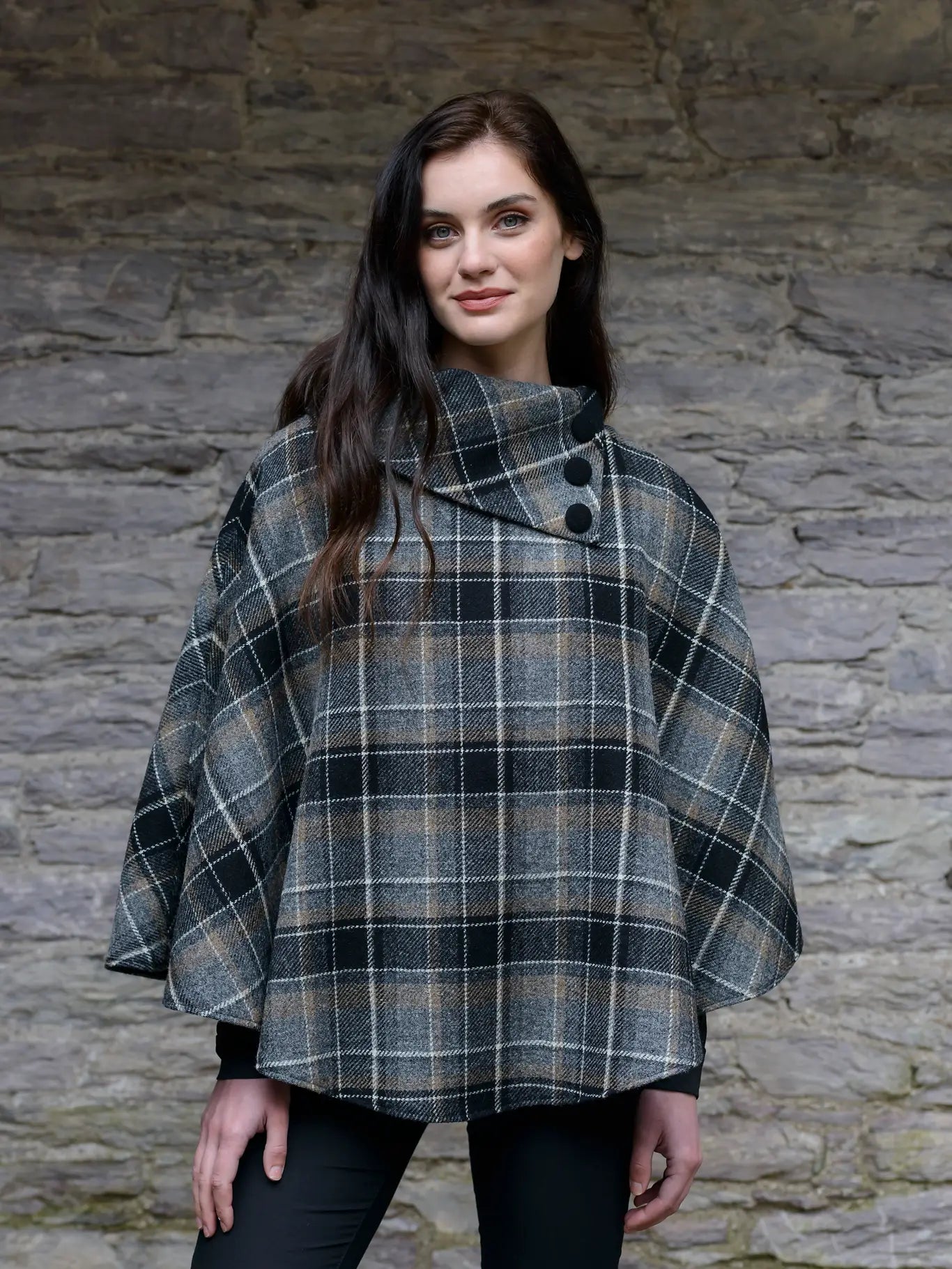 Woman wearing a plaid poncho against a stone wall background