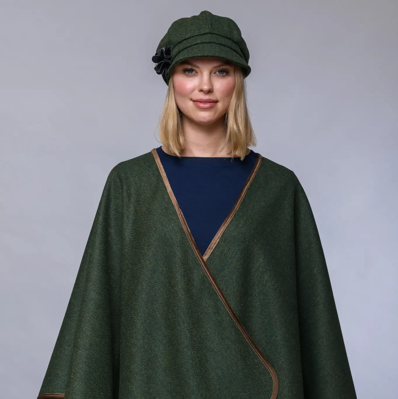 Woman wearing a green cape and matching hat against a gray background