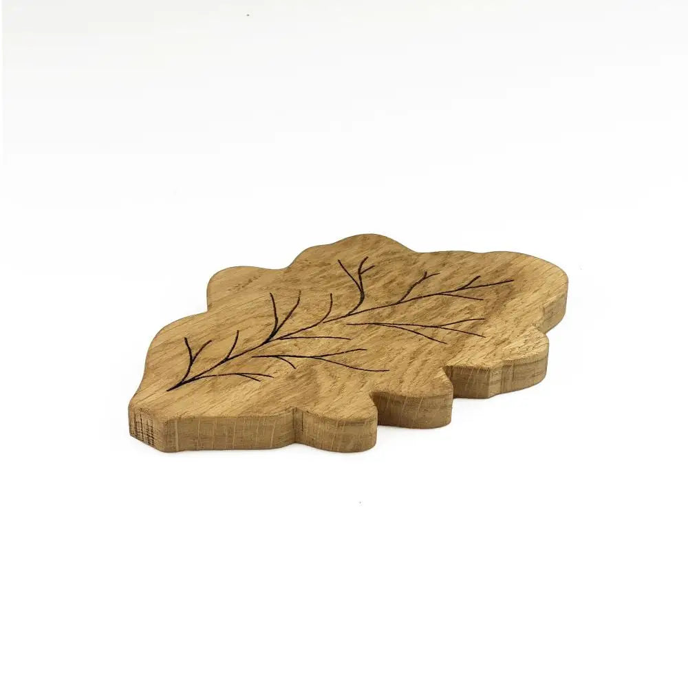 Wooden leaf-shaped cutting board with engraved branch design on a white background