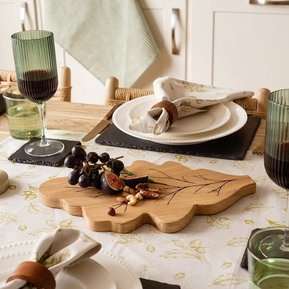 Dining table setting with a wooden cutting board, glasses, and plates.