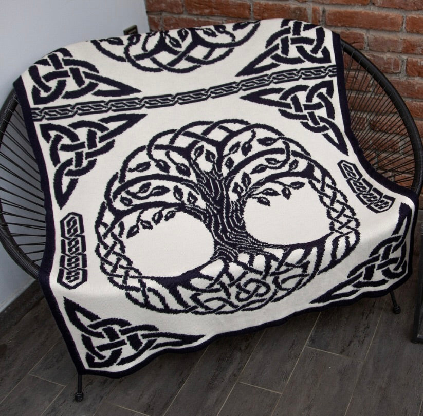 Blanket with Tree of Life design and Celtic knots on a chair against a brick wall.