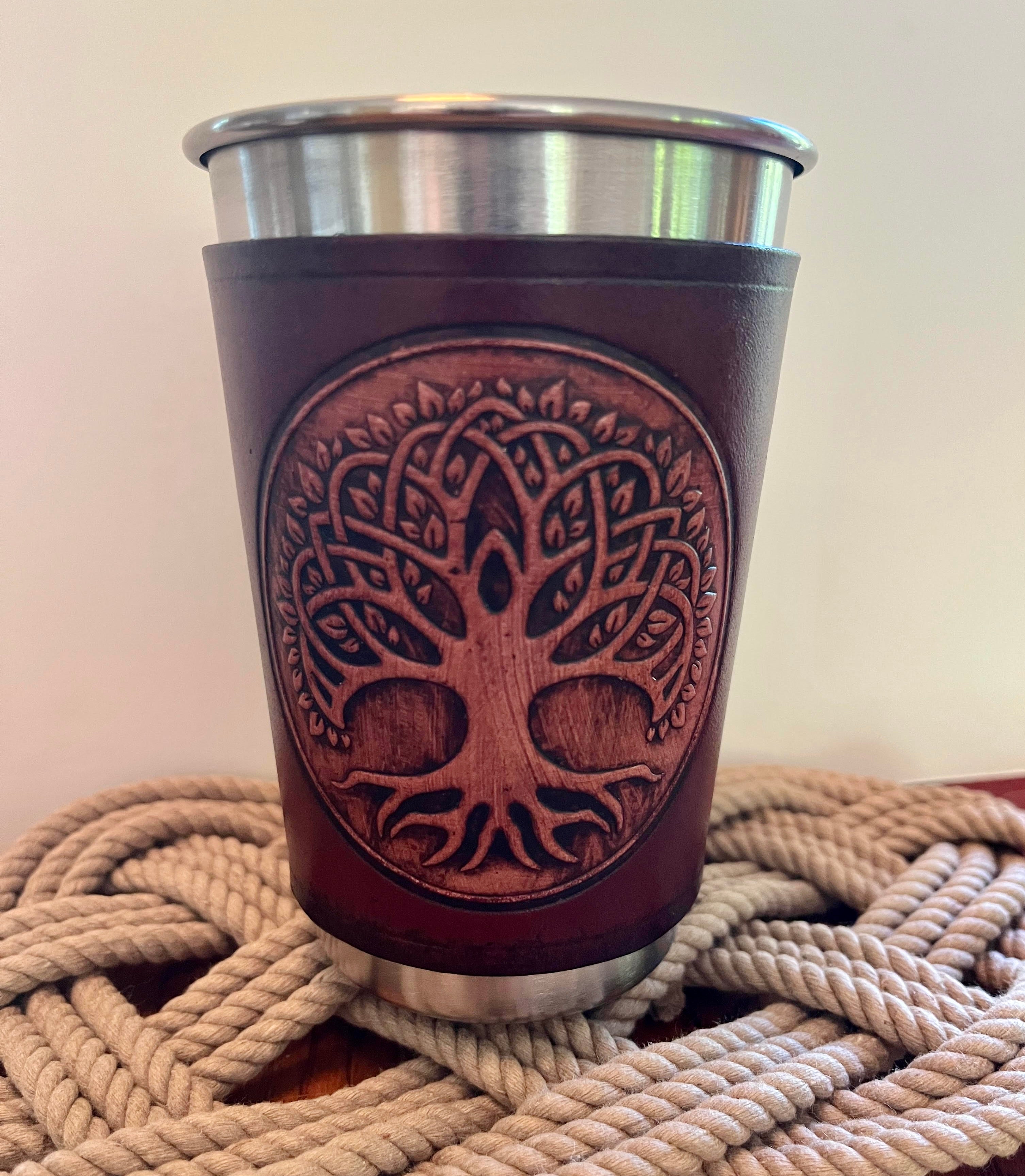 Brown leather cup with tree design on a metal base, placed on a woven surface.