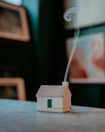 Small house-shaped incense burner with smoke emerging on a table.
