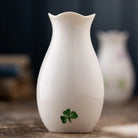 White vase with a green clover design on a wooden surface