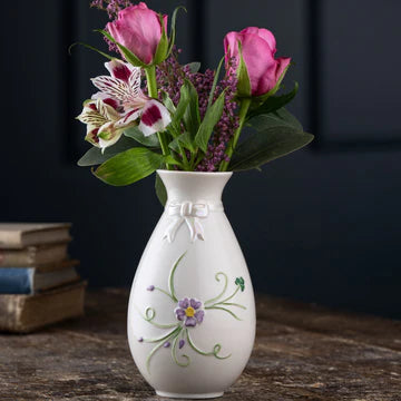 White decorative vase with floral design on a wooden surface against a dark background