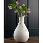 White ceramic vase with floral design on a wooden surface against a dark background