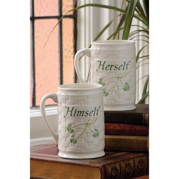 Two white mugs with 'Herself' and 'Himself' text on a wooden surface with books and a plant in the background.