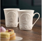 Two white ceramic mugs with embossed designs on a wooden surface.