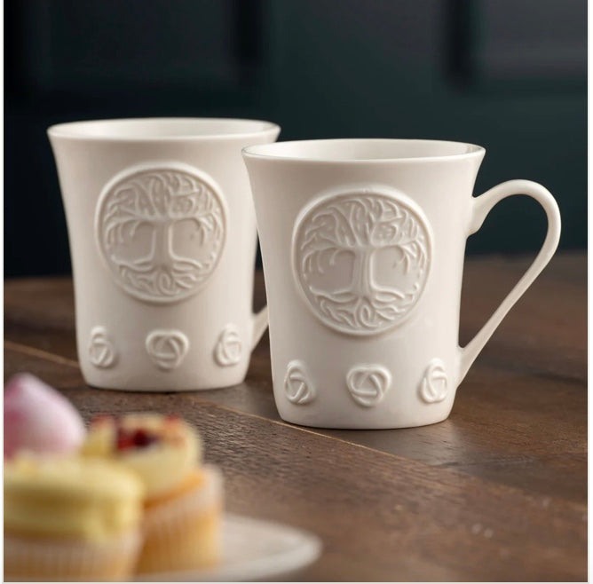 Two white ceramic mugs with embossed designs on a wooden surface.