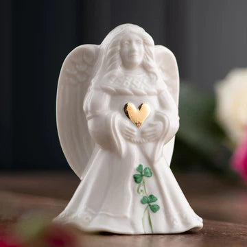 White angel figurine holding a gold heart on a wooden surface with a dark background