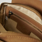 Close-up of a brown leather bag with a zipper, showing brand logo.