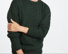 Person wearing a dark green cable knit sweater on a light gray background