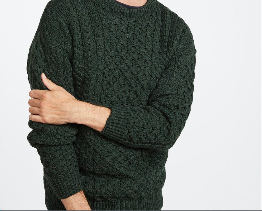 Person wearing a dark green cable knit sweater on a light gray background