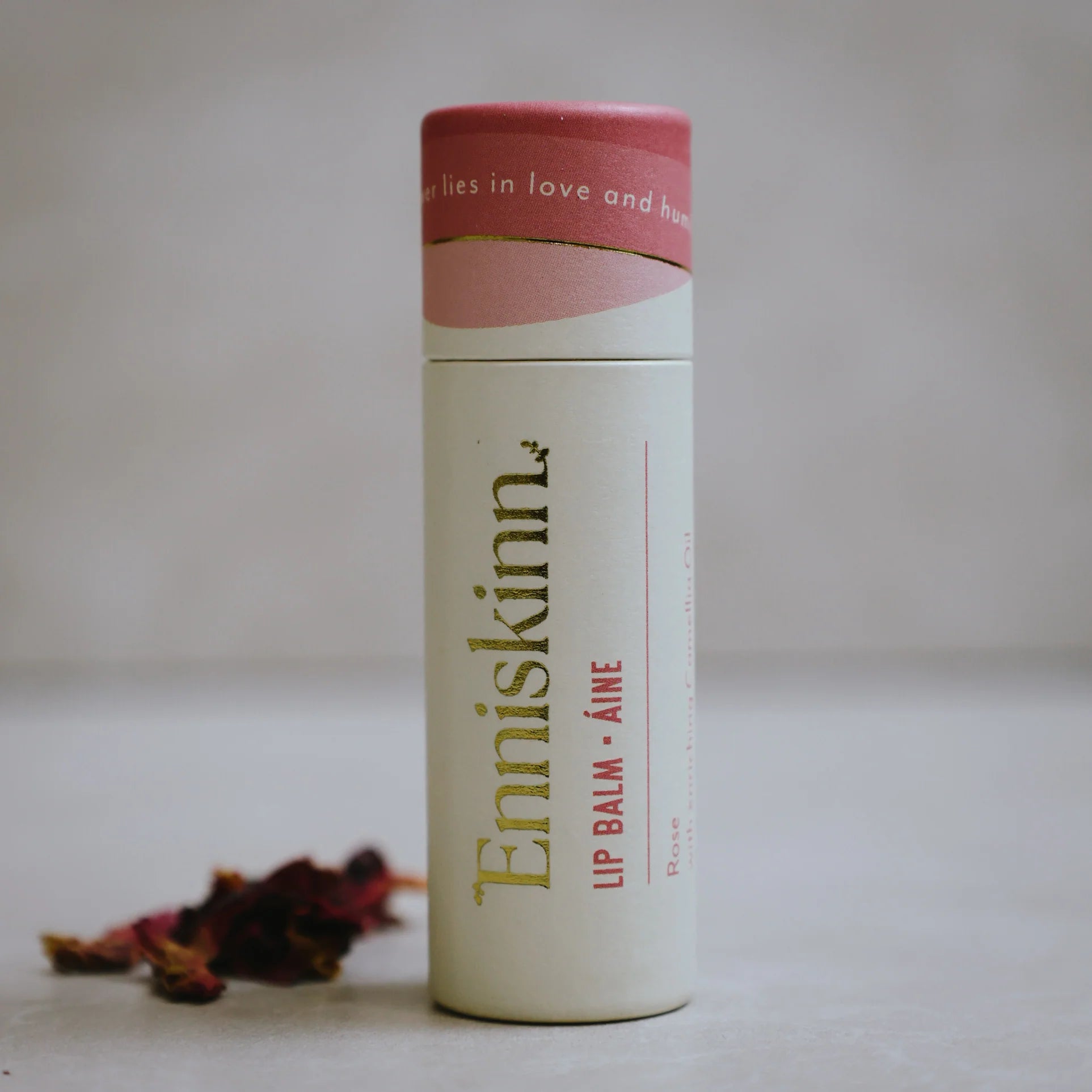 Lip balm container with pink cap and visible branding on a neutral background