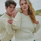Two people wearing cream-colored Irish knitted sweaters on a beach.