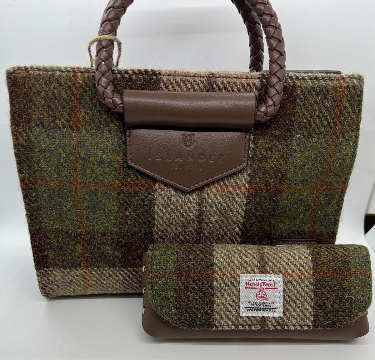 A small tweed handbag with braided brown handles and a matching zip pouch, both in a brown, green, and beige plaid pattern. The front of the bag has a brown leather tab embossed with 'ISLANDER tweed'.