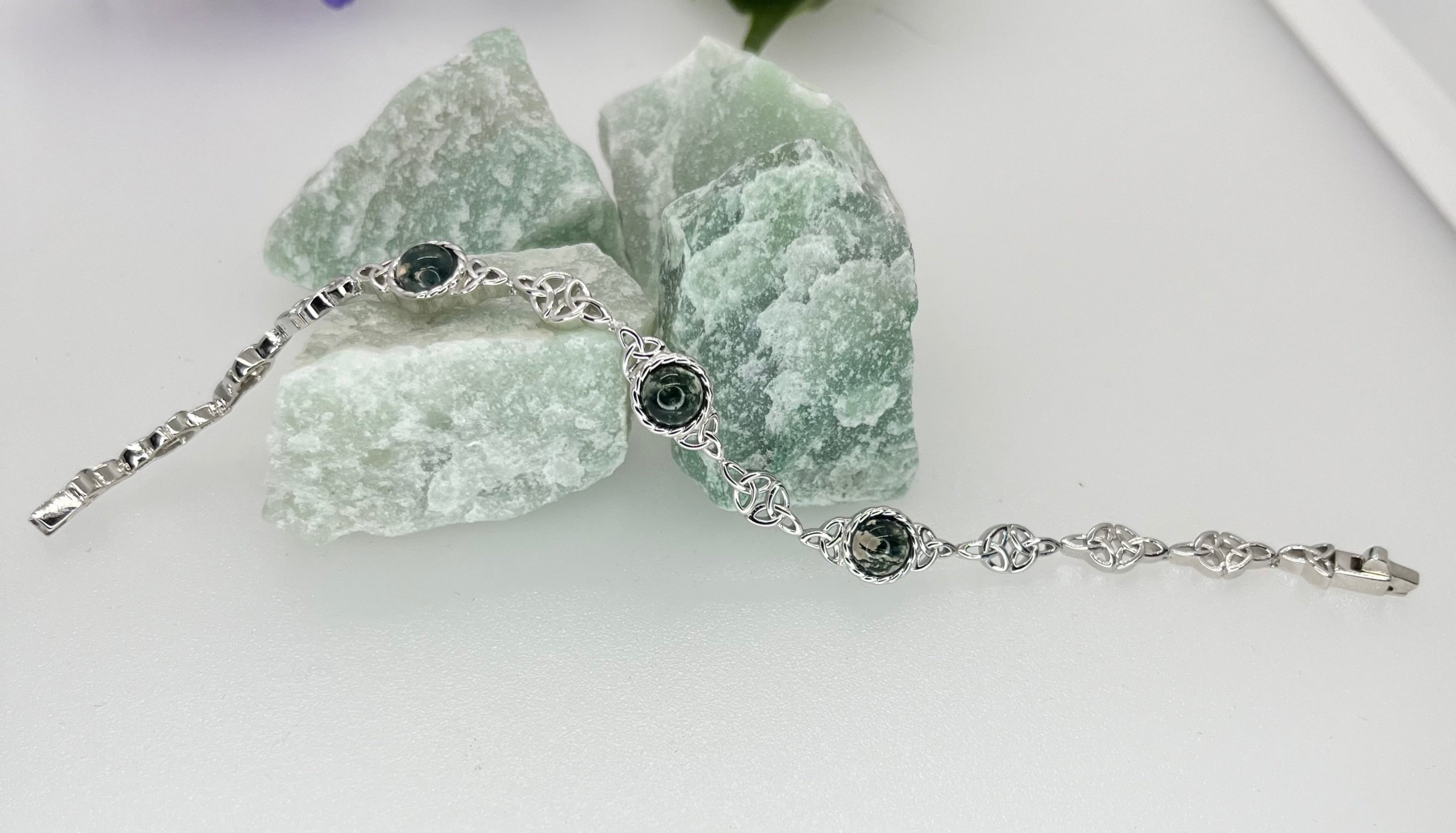 Silver bracelet with green stones on a white surface with green crystals in the background