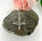 Silver necklace with a star-shaped pendant on a rock with a pink flower in the background